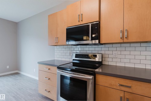Kitchen featuring light wood cabinetry, dark countertops, a white subway tile backsplash, and stainless steel appliances - 7827 18 Avenue, Edmonton, AB - Indoor Photo Showing Kitchen