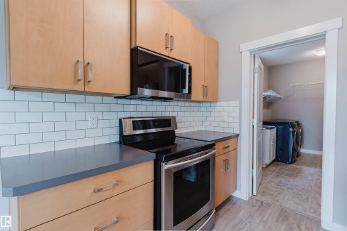 Kitchen featuring light wood-finish cabinetry, stainless steel appliances, dark countertops, and a white subway tile backsplash - 7827 18 Avenue, Edmonton, AB - Indoor Photo Showing Kitchen