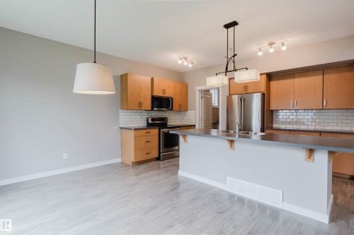 Open-concept kitchen featuring light wood cabinetry, stainless steel appliances, a subway tile backsplash, and a central island with an integrated sink - 7827 18 Avenue, Edmonton, AB - Indoor Photo Showing Kitchen