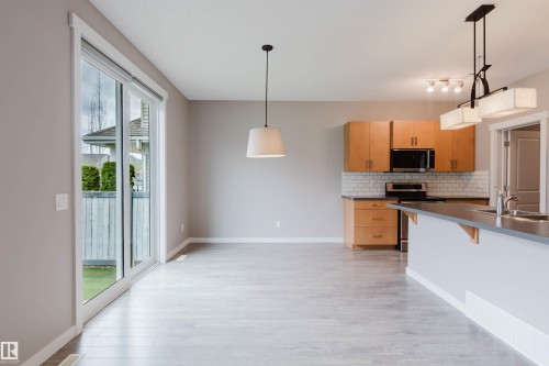 Open-concept living area featuring light wood-finish flooring, a contemporary kitchen with light wood cabinetry, white subway tile backsplash, and stainless steel appliances - 7827 18 Avenue, Edmonton, AB - Indoor Photo Showing Kitchen With Double Sink