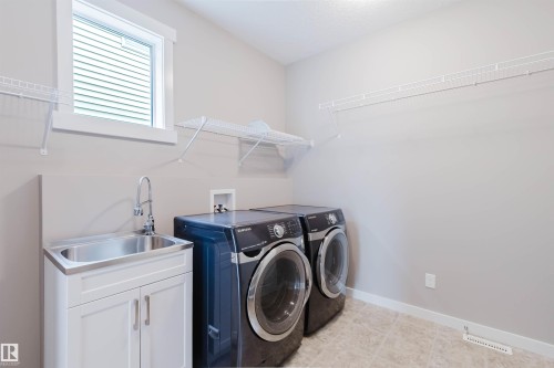 Dedicated laundry area featuring a stainless steel utility sink with a chrome faucet, white base cabinet, and light-toned tile flooring - 7827 18 Avenue, Edmonton, AB - Indoor Photo Showing Laundry Room