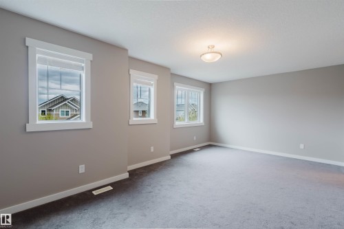 Spacious room featuring three windows with white trim, neutral gray wall paint, gray carpeting, and a flush-mount ceiling light fixture - 7827 18 Avenue, Edmonton, AB - Indoor Photo Showing Other Room