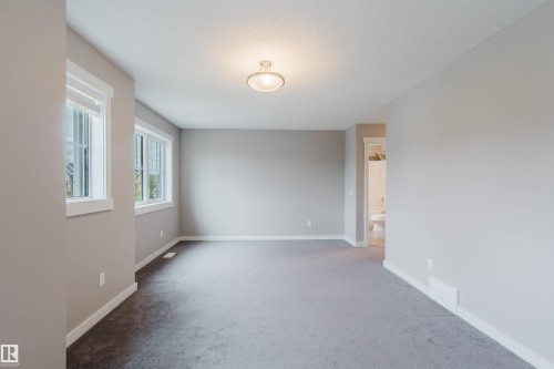 Spacious room featuring neutral gray carpeting and walls, multiple windows with white trim, and a ceiling-mounted light fixture - 7827 18 Avenue, Edmonton, AB - Indoor Photo Showing Other Room