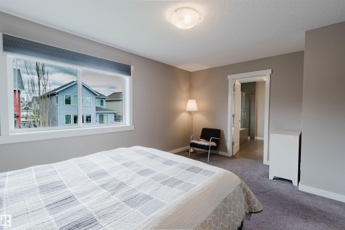 Bedroom featuring a wide window with white trim, neutral-toned walls, and grey carpeting - 7827 18 Avenue, Edmonton, AB - Indoor Photo Showing Bedroom
