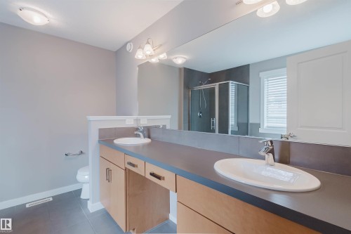 Bathroom featuring a dual vanity with undermount sinks, wood-finish cabinetry, and a large wall-mounted mirror - 7827 18 Avenue, Edmonton, AB - Indoor Photo Showing Bathroom