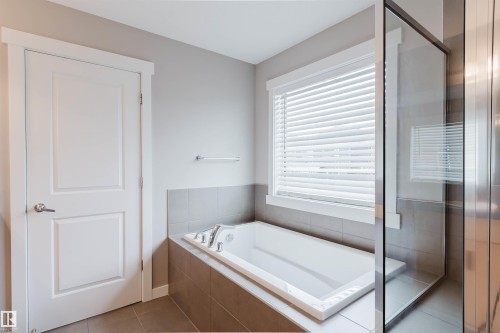 Soaking tub with a tiled surround, framed window with blinds, and glass shower enclosure - 7827 18 Avenue, Edmonton, AB - Indoor Photo Showing Bathroom