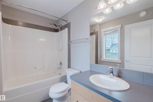 Bathroom featuring a white tub/shower combination with a chrome showerhead, a toilet, and a light wood-finish vanity with a gray countertop and an oval undermount sink - 7827 18 Avenue, Edmonton, AB - Indoor Photo Showing Bathroom