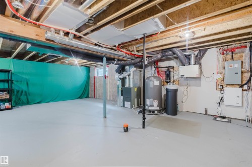 Unfinished basement with exposed ceiling joists, concrete floor, water heater, water softener, and visible utility systems - 7827 18 Avenue, Edmonton, AB - Indoor Photo Showing Basement