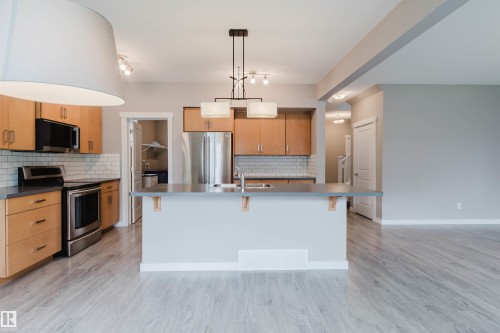 Kitchen featuring wood-finish cabinetry, stainless steel appliances, subway tile backsplash, and a central island with an integrated sink - 7827 18 Avenue, Edmonton, AB - Indoor Photo Showing Kitchen With Double Sink