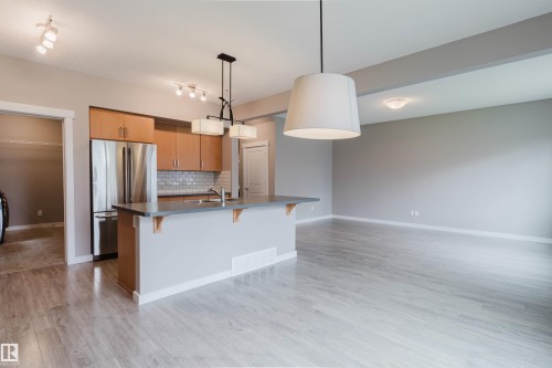 Open-concept living space featuring wood-finish flooring, a kitchen island with integrated sink, stainless steel refrigerator, and recessed lighting - 7827 18 Avenue, Edmonton, AB - Indoor Photo Showing Kitchen With Double Sink