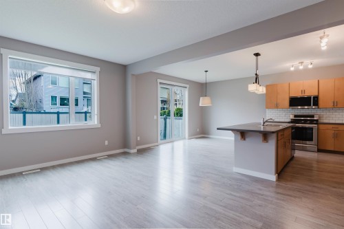 Open-concept living space featuring wood-finish flooring, a kitchen island with a sink, stainless steel appliances, and light wood cabinetry with a subway tile backsplash - 7827 18 Avenue, Edmonton, AB - Indoor Photo Showing Kitchen