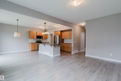 Kitchen and living area featuring wood-finish flooring, light grey walls, light wood cabinetry, a stainless steel refrigerator, and modern pendant lighting - 7827 18 Avenue, Edmonton, AB - Indoor Photo Showing Kitchen
