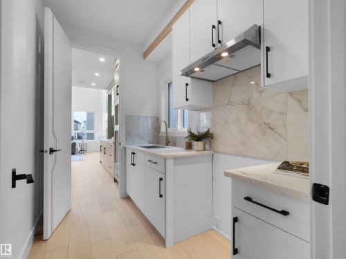 Modern kitchen featuring light wood-finish flooring, white cabinetry with black hardware, and stone-finish countertops - 43 Eldridge Point(E), St. Albert, AB - Indoor Photo Showing Kitchen