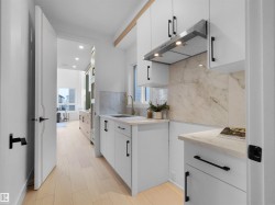 Modern kitchen featuring light wood-finish flooring, white cabinetry with black hardware, and stone-finish countertops - 