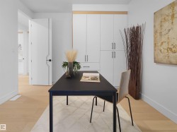 Dedicated office space featuring built-in cabinetry with modern hardware, light wood-finish flooring, and a contemporary door with a distinct linear design - 