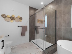 Modern bathroom featuring a frameless glass shower enclosure with matte black hardware, large format grey wall tiles, and white marble-look floor tiles - 