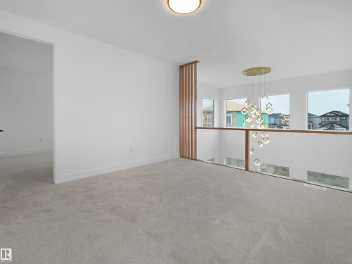 Open concept hallway featuring modern chandelier, light neutral carpet, white walls, and a wood slat accent wall - 43 Eldridge Point(E), St. Albert, AB - Indoor Photo Showing Other Room
