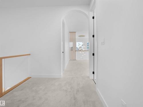 Arched entryway leading to a carpeted hallway with a glass and wood railing - 43 Eldridge Point(E), St. Albert, AB - Indoor Photo Showing Other Room