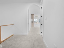Arched entryway leading to a carpeted hallway with a glass and wood railing - 