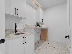 Bright utility space featuring white cabinetry with matte black hardware, a stainless steel sink with a matte black faucet, and stone-finish countertops - 