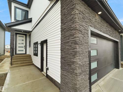 Exterior featuring stacked stone accents, horizontal siding, a contemporary front entry door with obscure glass inserts, a black garage door with frosted glass panels, and a concrete walkway - 43 Eldridge Point(E), St. Albert, AB - Outdoor