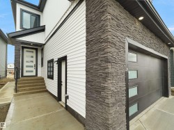 Exterior featuring stacked stone accents, horizontal siding, a contemporary front entry door with obscure glass inserts, a black garage door with frosted glass panels, and a concrete walkway - 