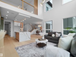 Two-story living area with high ceilings, large windows, light wood-finish flooring, and a contemporary kitchen island with a waterfall countertop - 