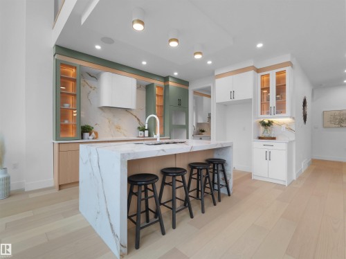 Gourmet kitchen featuring a waterfall island with a built-in sink and seating for four, two-tone cabinetry, a full height stone backsplash, and recessed and pendant lighting - 43 Eldridge Point(E), St. Albert, AB - Indoor Photo Showing Kitchen With Upgraded Kitchen