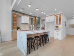 Gourmet kitchen featuring a waterfall island with a built-in sink and seating for four, two-tone cabinetry, a full height stone backsplash, and recessed and pendant lighting - 