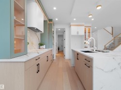 Gourmet kitchen featuring a waterfall island with an undermount sink, light wood-finish cabinetry, marble-patterned countertops and backsplash, a contemporary range hood, and recessed lighting - 