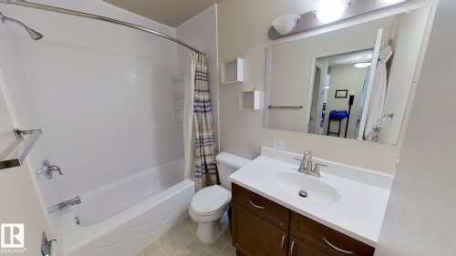 Bathroom featuring a white integrated tub and shower unit, a vanity with a white countertop and undermount sink, brushed nickel faucet, a dark wood-finish cabinet, and a large wall-mounted mirror - 401 10326 117 Street, Edmonton, AB - Indoor Photo Showing Bathroom