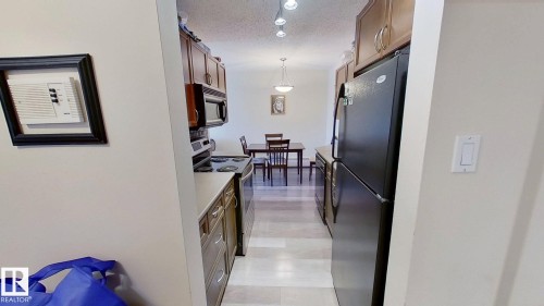 Galley kitchen featuring wood-finish cabinetry, stainless steel appliances, and wood-finish flooring - 401 10326 117 Street, Edmonton, AB - Indoor Photo Showing Other Room