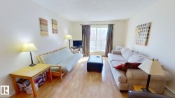 Spacious living area featuring wood-finish flooring, light neutral wall tones, and a large window with vertical blinds and drapery - 