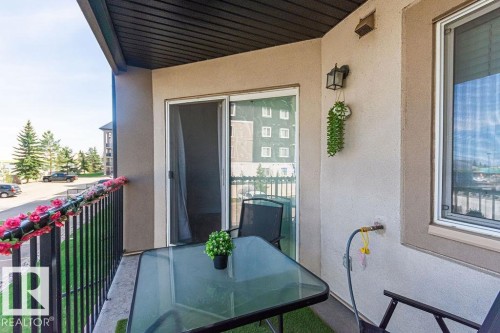 Private balcony featuring a black metal railing, stucco exterior, and a sliding glass door with screen - 214 13005 140 Avenue, Edmonton, AB - Outdoor With Exterior