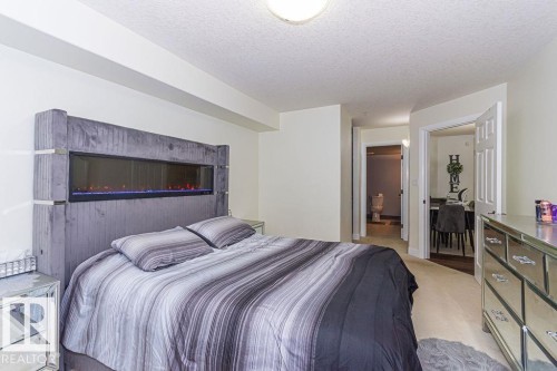 Bedroom featuring a built-in linear electric fireplace, light-toned wall paint, and overhead lighting - 214 13005 140 Avenue, Edmonton, AB - Indoor Photo Showing Bedroom