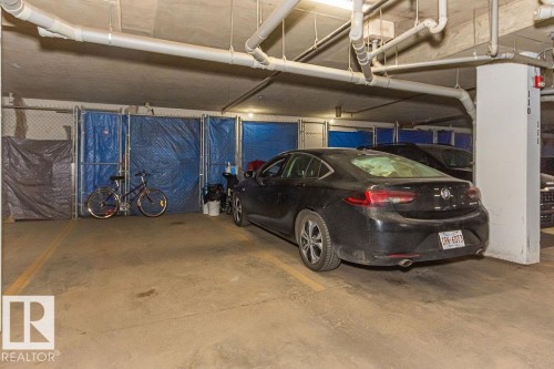 Dedicated parking space within a concrete garage structure, featuring overhead exposed piping and a support column - 214 13005 140 Avenue, Edmonton, AB - Indoor Photo Showing Garage