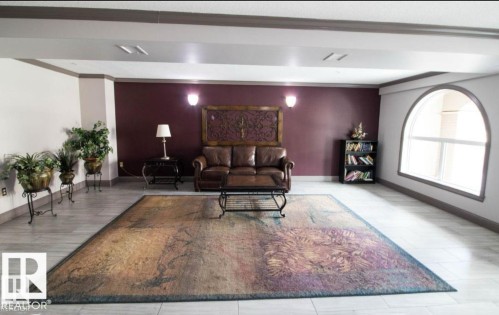 Spacious interior featuring light-toned tile flooring, a prominent arched window, and a built-in bookshelf - 214 13005 140 Avenue, Edmonton, AB - Indoor