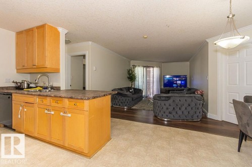 Open-concept living area featuring distinct flooring zones: light-toned tile in the kitchen and wood-finish flooring in the main living space - 214 13005 140 Avenue, Edmonton, AB - Indoor Photo Showing Kitchen