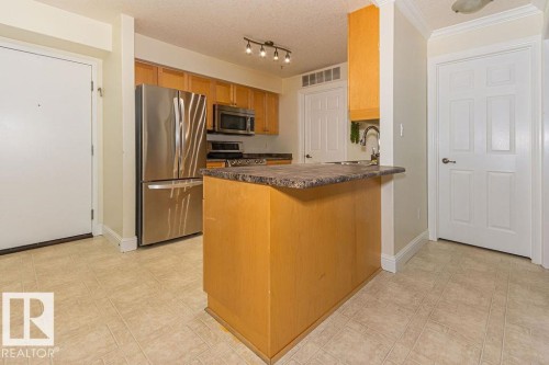 Kitchen featuring light wood cabinetry, stone-finish countertops, and stainless steel appliances - 214 13005 140 Avenue, Edmonton, AB - Indoor Photo Showing Kitchen