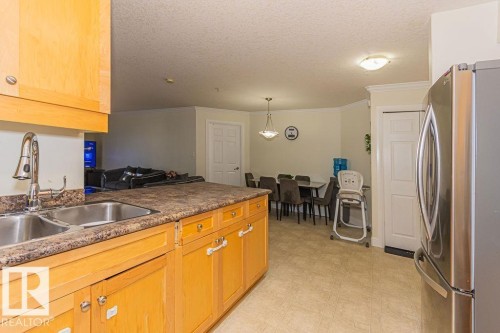 Kitchen with wood-finish cabinetry, a double basin stainless steel sink, and a textured countertop - 214 13005 140 Avenue, Edmonton, AB - Indoor Photo Showing Kitchen With Double Sink