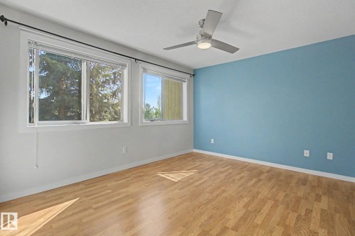 Room featuring wood-finish flooring, a contemporary ceiling fan with integrated lighting, a contrasting accent wall, and multiple windows with blinds - 204 278 Suder Greens Drive, Edmonton, AB - Indoor Photo Showing Other Room