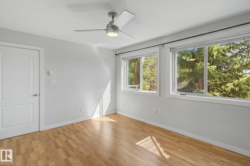 Bright room with wood-finish flooring, a modern ceiling fan, and multiple windows - 204 278 Suder Greens Drive, Edmonton, AB - Indoor Photo Showing Other Room
