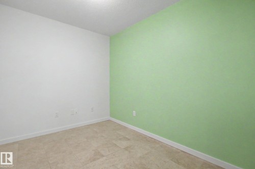 Neutral-toned tile flooring complements a green accent wall and crisp white baseboards - 204 278 Suder Greens Drive, Edmonton, AB - Indoor Photo Showing Other Room