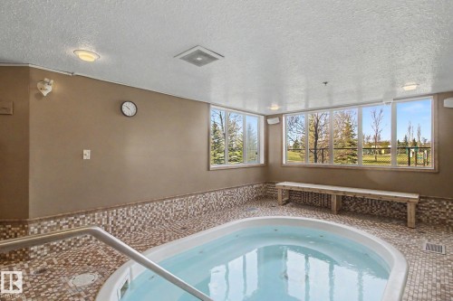Indoor spa area featuring an in-ground hot tub with metal handrails, surrounded by mosaic tile flooring and wainscoting - 204 278 Suder Greens Drive, Edmonton, AB - Indoor Photo Showing Other Room