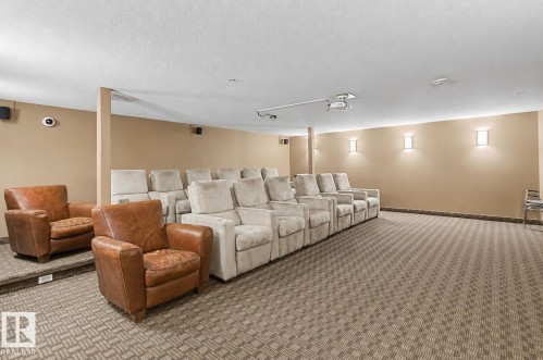 Dedicated screening room featuring tiered seating, patterned carpet, and wall-mounted sconces - 204 278 Suder Greens Drive, Edmonton, AB - Indoor