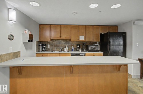 Kitchen featuring a light-toned countertop, wood-finish cabinetry, black appliances, and a tiled backsplash - 204 278 Suder Greens Drive, Edmonton, AB - Indoor Photo Showing Kitchen