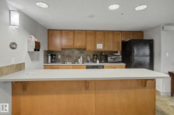Kitchen featuring a light-toned countertop, wood-finish cabinetry, black appliances, and a tiled backsplash - 