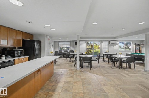 Community room featuring a full kitchen with wood cabinetry and black appliances, a spacious dining area, a recreation zone with a billiards table, expansive windows, and recessed lighting - 204 278 Suder Greens Drive, Edmonton, AB - Indoor