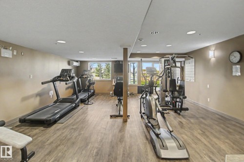 Spacious fitness area featuring wood-finish flooring, recessed lighting, and large windows - 204 278 Suder Greens Drive, Edmonton, AB - Indoor Photo Showing Gym Room
