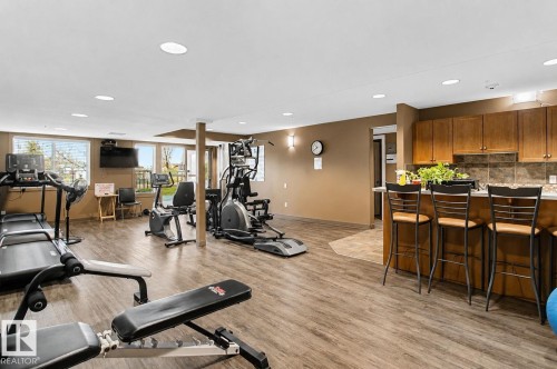 Fitness center with wood-finish flooring, recessed lighting, and a snack bar featuring wood cabinetry and a tile backsplash - 204 278 Suder Greens Drive, Edmonton, AB - Indoor Photo Showing Gym Room